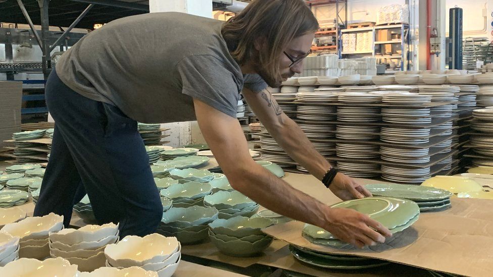 A worker stacks ceramic plates in a factory