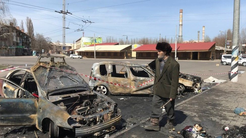 A man walks past burned cars at the site of a missile strike, at a rail station