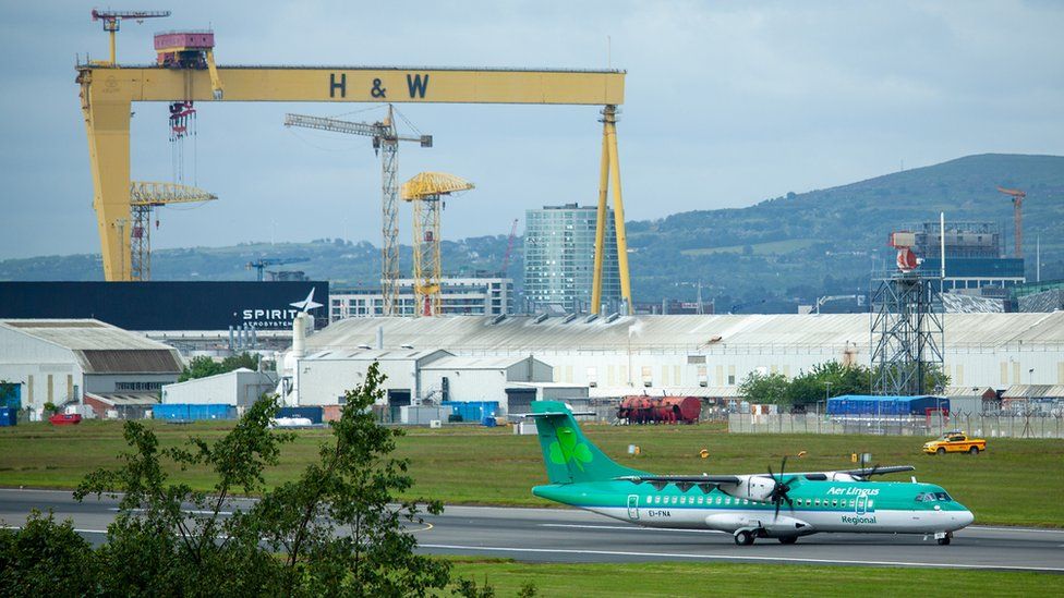 An Aer Lingus plane landing at Belfast City Airport with a Harland and Wolff shipyard crane in the background
