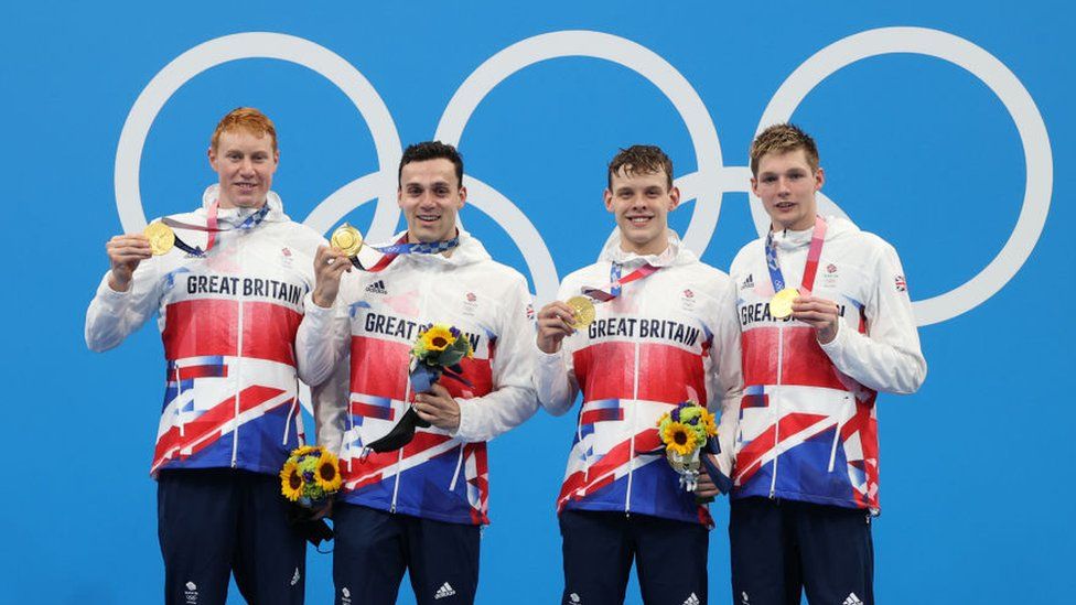 Four men standing together holding up their Olympic medals