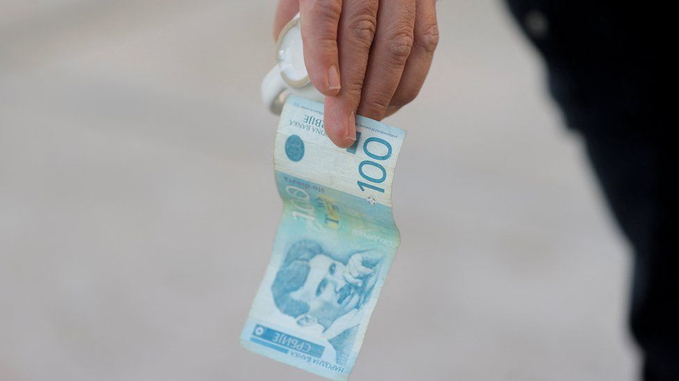 A man holds a dinar currency and a coffee cup in Mitrovica, Kosovo, February 1, 2024