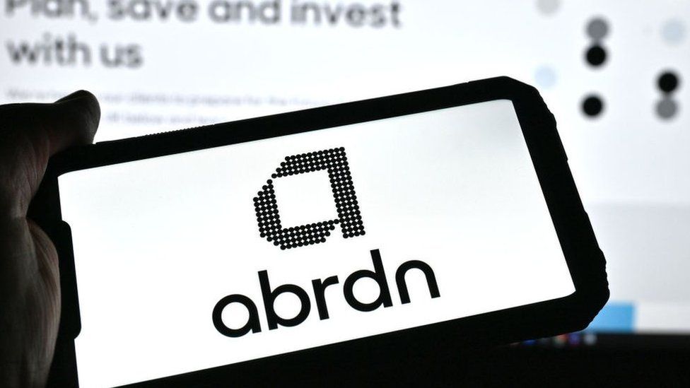 Person holding a phone with the Abrdn logo on it