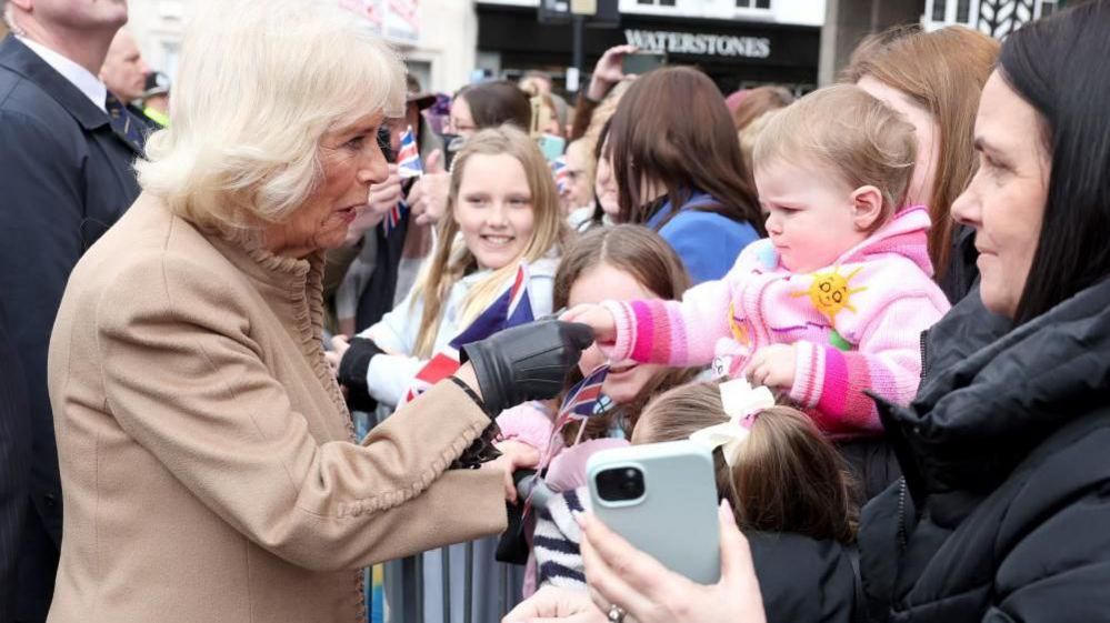 The Queen shakes a baby's hand.