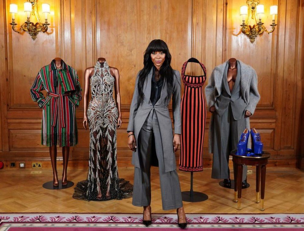 Naomi Campbell stands in front of mannequins wearing her outfits