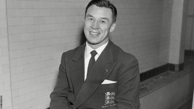 A smiling Frank Soo poses in a shirt, tie and a blazer with three lions on the breast pocket