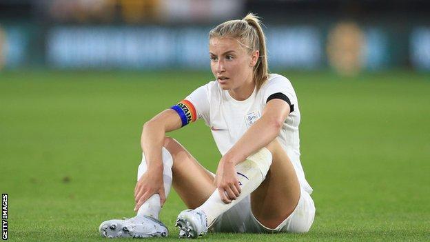 Leah Williamson, England captain, sits on the turf.
