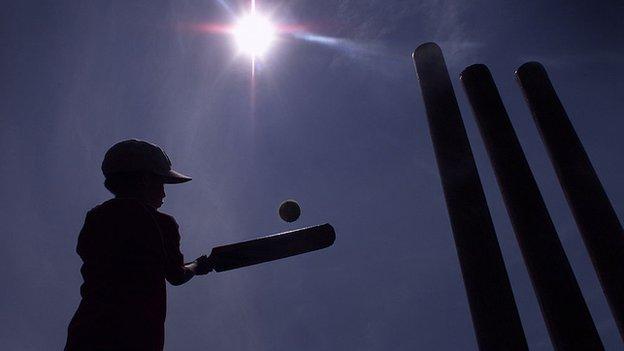 A young boy plays cricket in the sun