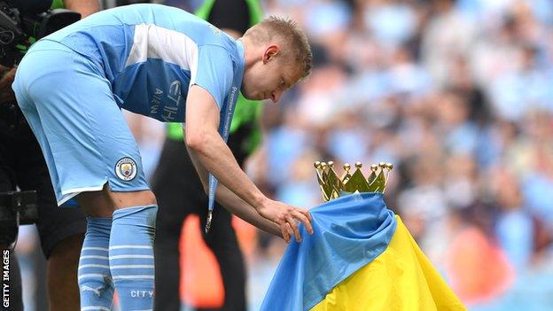 Manchester City's Oleksandr Zinchenko wraps a Ukraine flag around the Premier League trophy