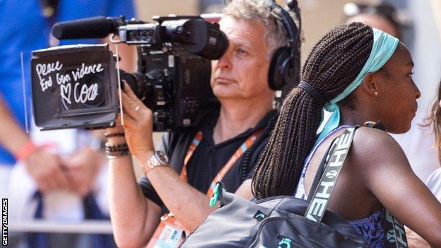 Coco Gauff walks past a cameraman after writing 'peace - end gun violence' on the lens