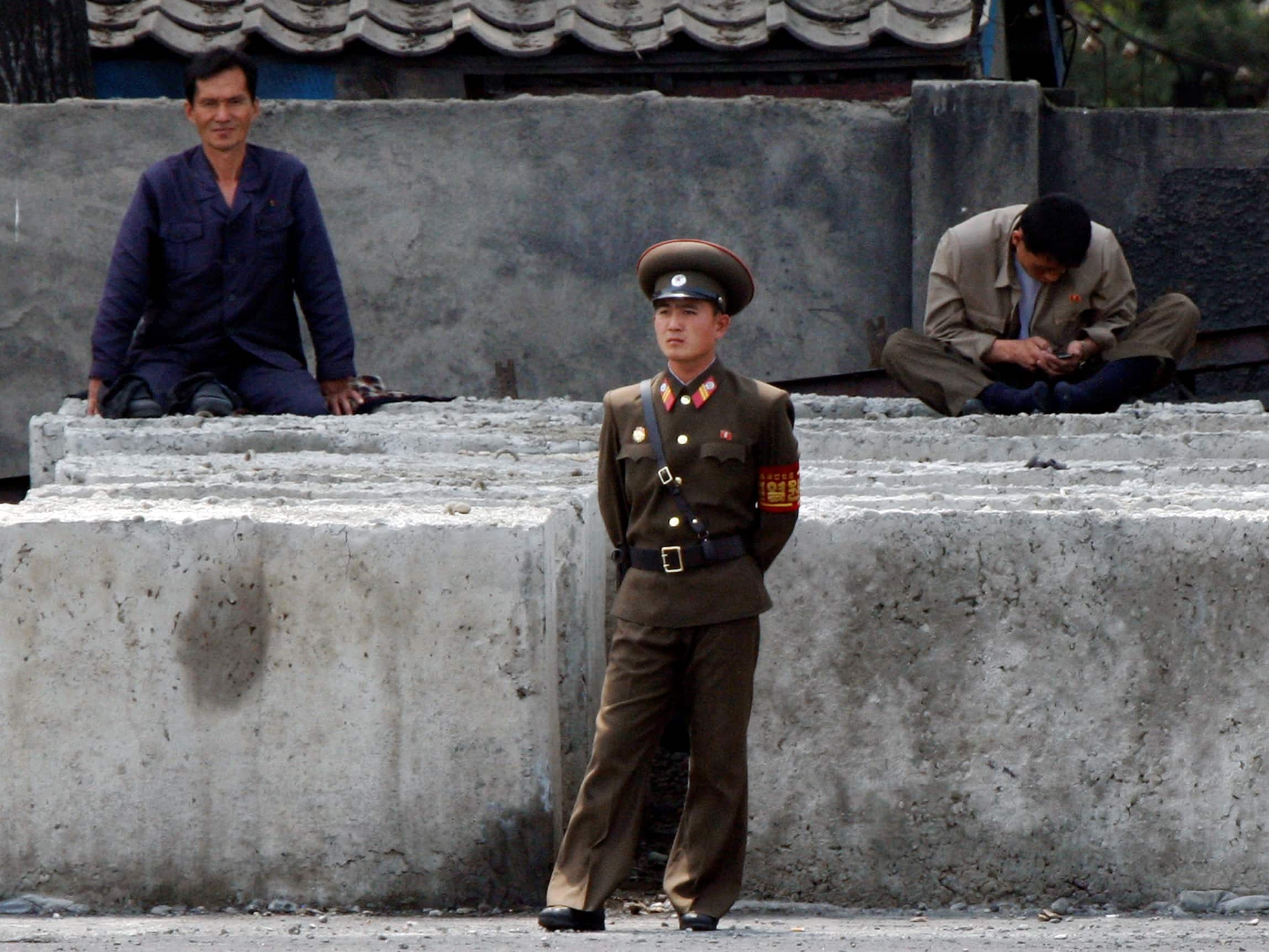 A North Korean worker checks his mobile phone as a soldier stands in front along the banks of Yalu River, 7 June 2013; using a mobile phone remains risky, as information that someone was seen doing this can be enough to spark an investigation, arrest, and abuse in detention, REUTERS/Jacky Chen