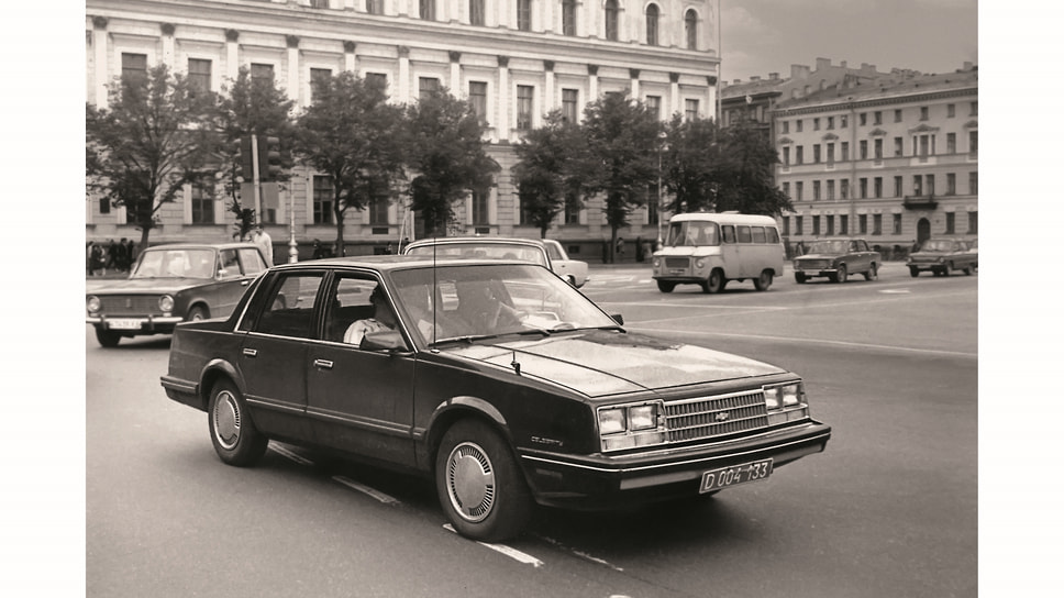Массовый и дешевый седан восьмидесятых Chevrolet Celebrity на Исаакиевской площади в Ленинграде. Дата снимка — 28 июля 1987 года. Позади плетется советский автопром: ВАЗ-2101 «Жигули», ГАЗ-24 «Волга», ЗАЗ-968М «Запорожец». И между ними едет польский микроавтобус Nysa. Кстати, в 1987 году производная от «Копейки» модель 21013 еще стояла на конвейере — ее прекратят выпускать только два года спустя. Задний план на сегодняшний день почти не изменился, как это часто бывает в Сакт-Петербурге
