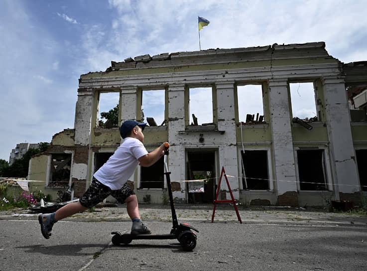 Мальчик катается на скутере перед уничтоженным зданием мэрии в городе Ахтырка в Сумской области