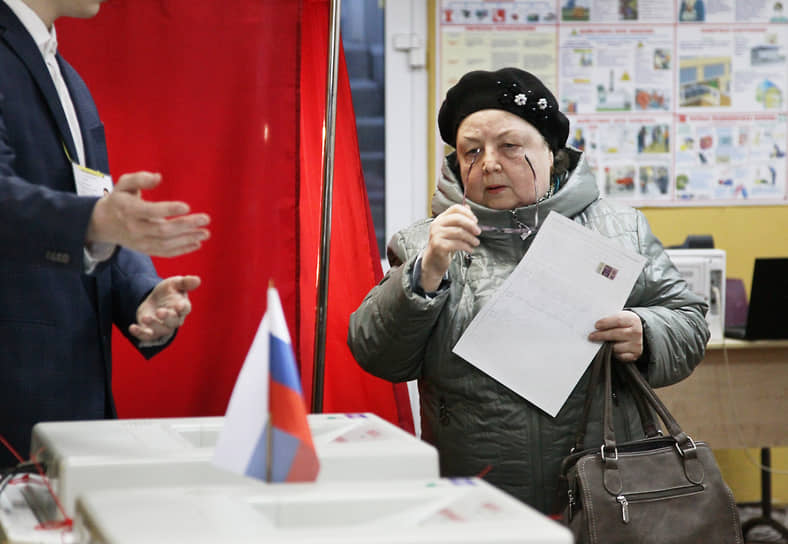 Женщина с бюллетенем подходит к урне для голосования
