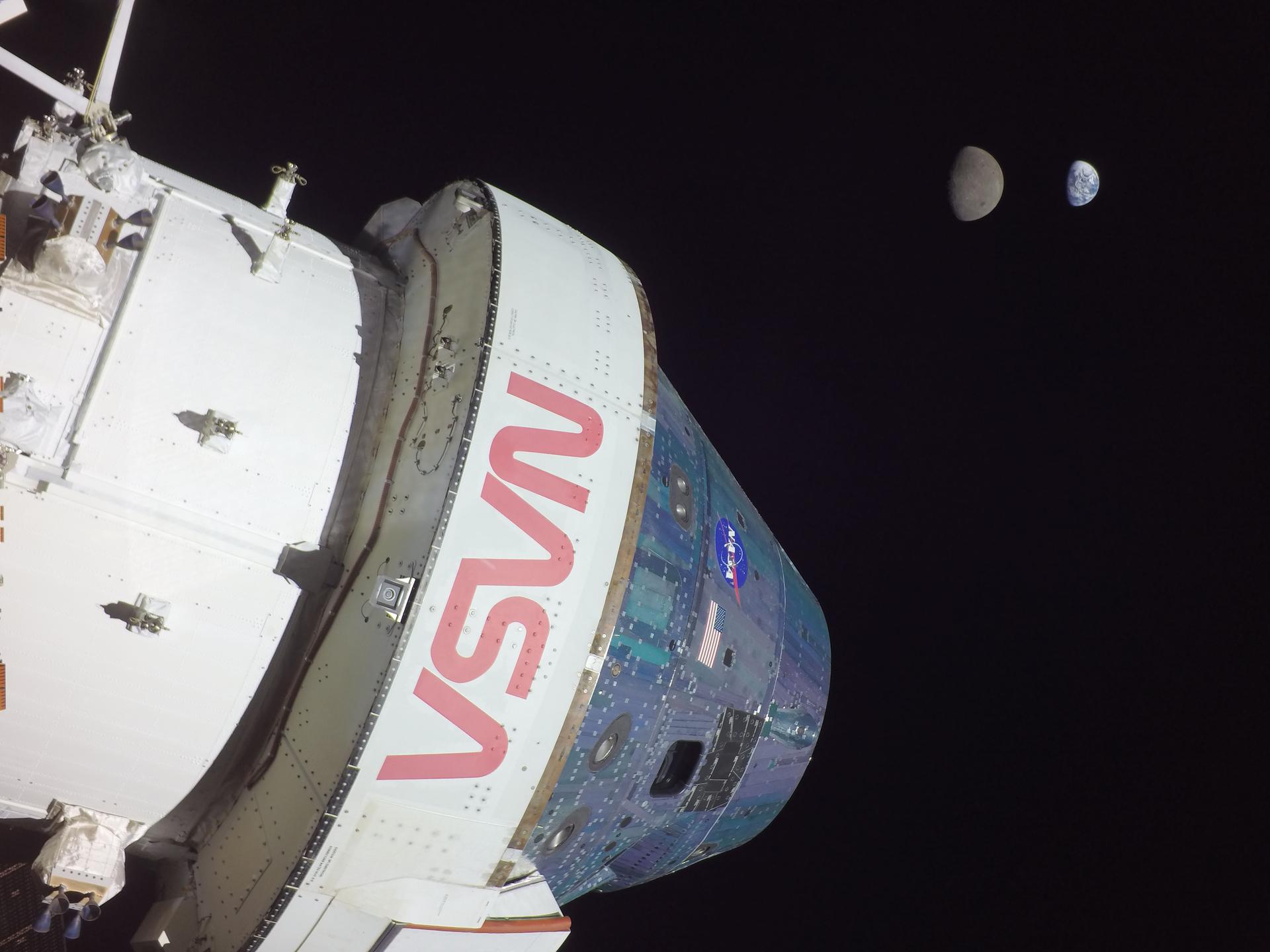 Photo taken from the Orion spacecraft on flight day 13 of the Artemis I flight test. The photo features Orion prominently in the foreground, with "NASA" written on the spacecraft in bold red letters. The Moon is seen in the background, with Earth even farther behind it. Orion reached its maximum distance from Earth during the Artemis I mission when it was 268,563 miles away from our home planet. Orion has now traveled farther than any other spacecraft built for humans.