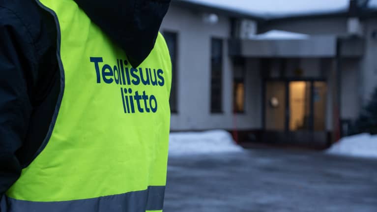 En person står utomhus med en reflexväst på sig. På ryggen står det Industrifacket på finska.
