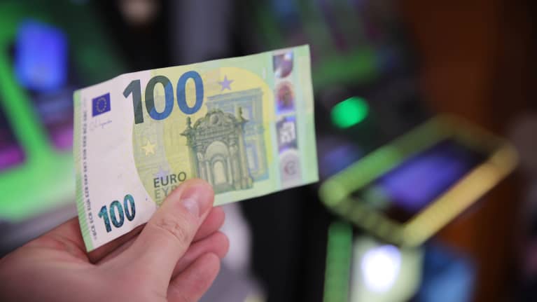Henkilö pitää sadan euron seteliä kädessään rahapeliautomaattien edessä.