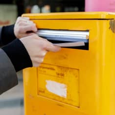 Photo shows a letter being put into a post box.