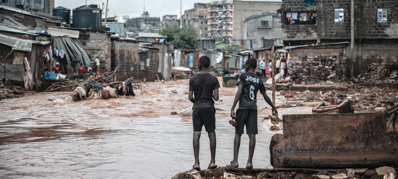 Menschen stehen am Ufer eines überfluteten Flusses in den Mathare-Slums in Nairobi.