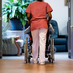 Eine Pflegerin schiebt einen Rollstuhl mit einer Bewohnerin durch einen Gang