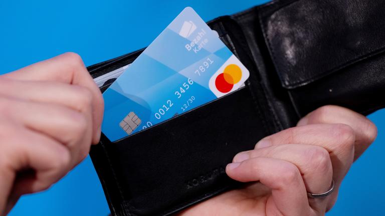 Eine Hand zieht eine Bezahlkarte aus einem Portemonnaie.