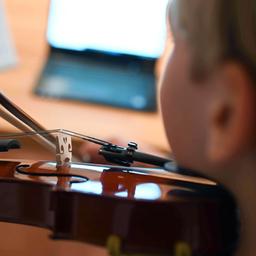 Ein Junge übt vor seinem Computer mit seiner Geige.