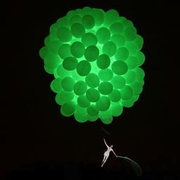 Eine Frau, befestigt an grün illuminierten Ballons, scheint zu schweben.
