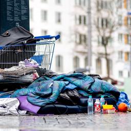 Ein Schlafsack und Kleidungsstücke liegen vor einem Einkaufswagen auf Pflastersteinen.
