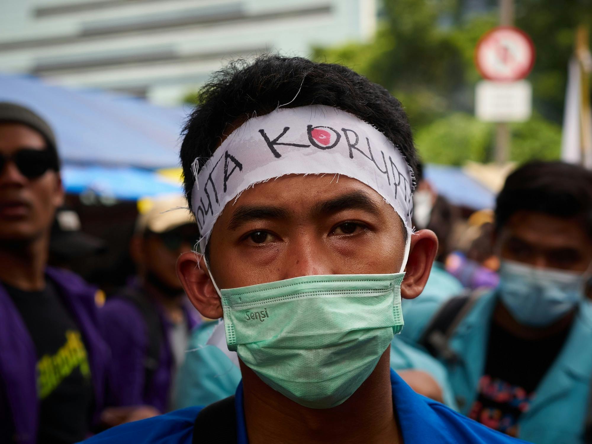 A man wearing a green mask looks right at the camera during a protest
