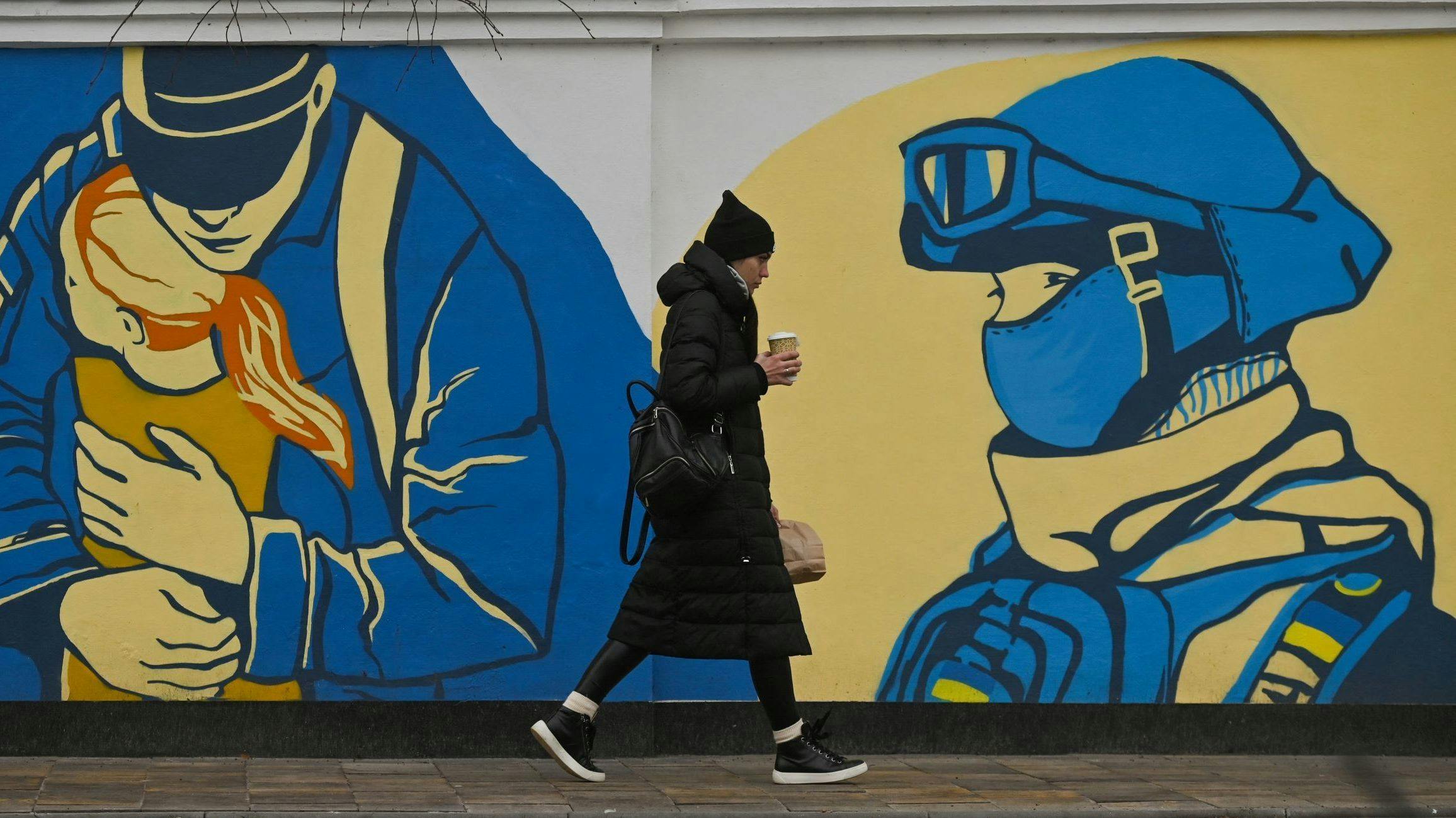 A woman walks past a mural in Ukraine depicting service people.