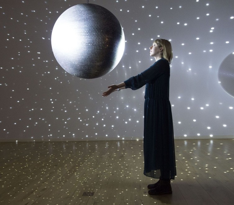 Katie Paterson looking at a mirror ball which is actively reflecting specs of light across the room