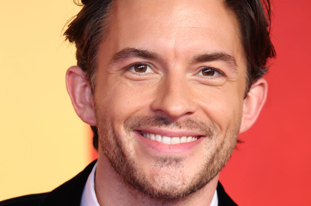 Man smiling at a red carpet event, wearing a black tuxedo with a bow tie