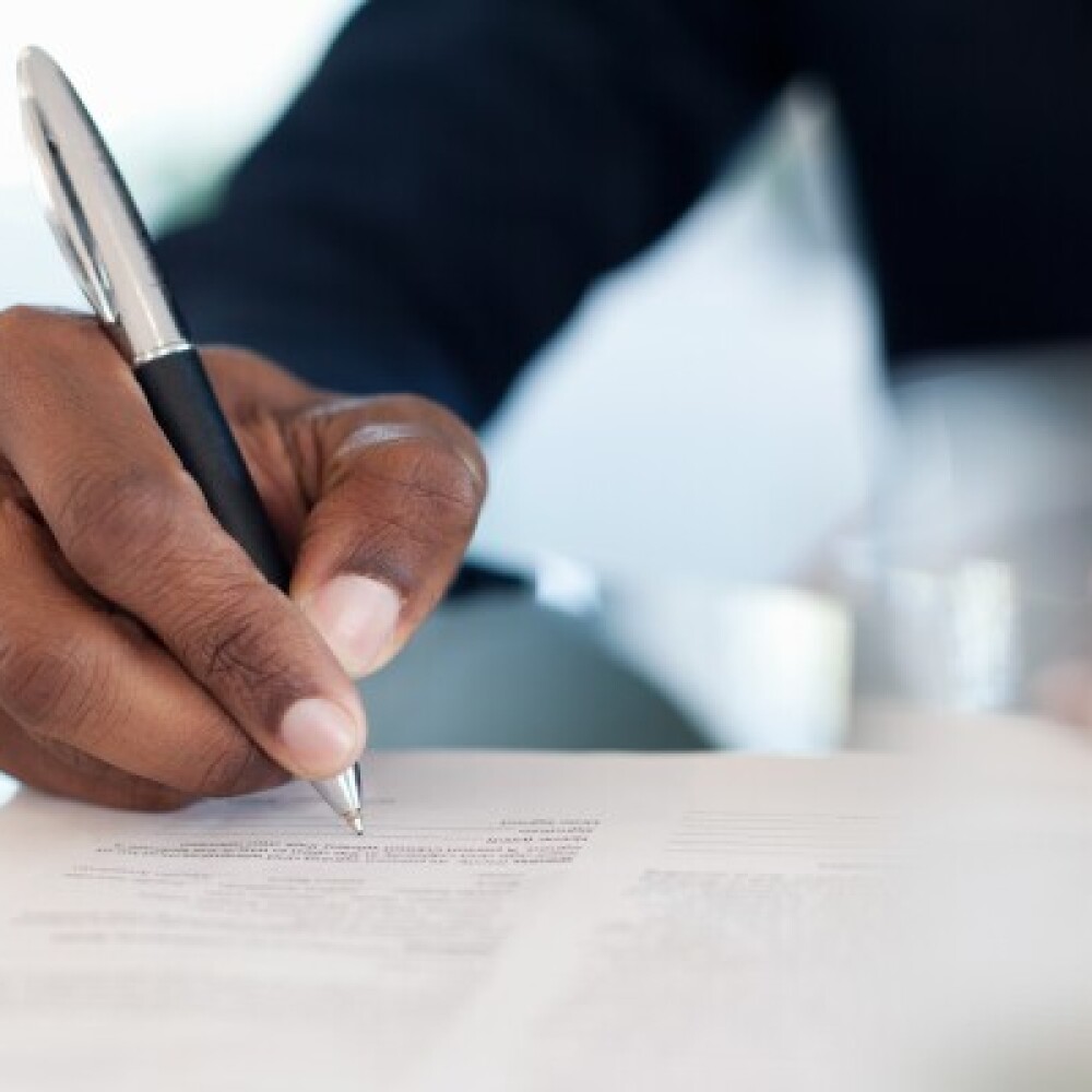 A close-up of a hand holding a pen and signing documents 