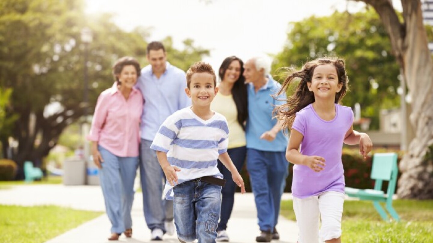 Two children smiling and running ahead of their family members on a sidewalk 