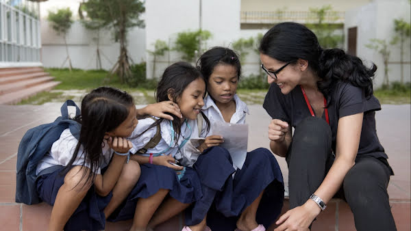 A woman smiling and sitting with three students outside