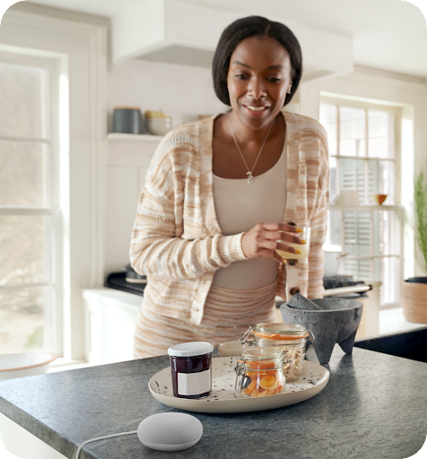 A person stands in a kitchen looking down at a smart device on the counter.