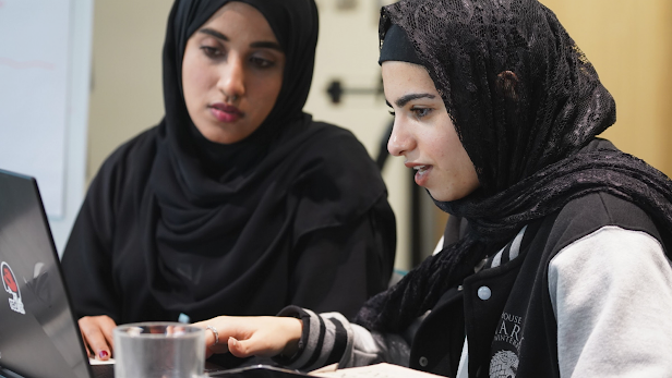 Two women in hijabs work together on a laptop