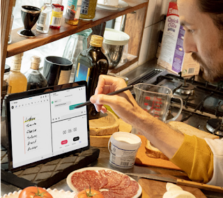 Man in a cluttered kitchen using a stylus pen to write shopping list on his Android tablet