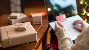 Woman using credit card to do online shopping on a laptop next to holiday gifts.