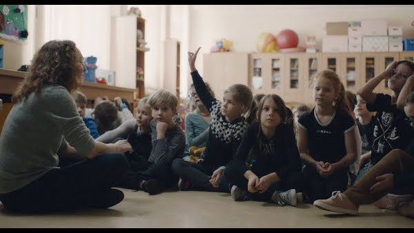 Young children sitting on the floor in a class room.