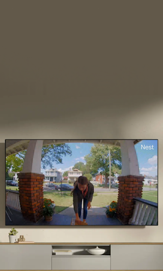 Un écran de télévision installé dans un salon montrant un livreur sur le perron qui fait signe à la sonnette vidéo.