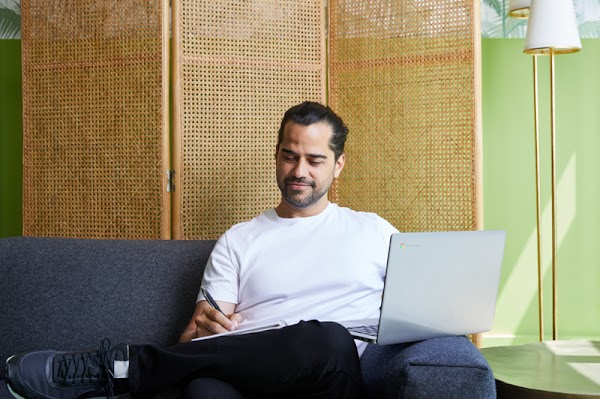 Alberto Villarubia, graduado del programa de Certificados Profesionanles de Google en Diseño de UX, sentado en un sofá azul mientras trabaja en su computadora portátil.