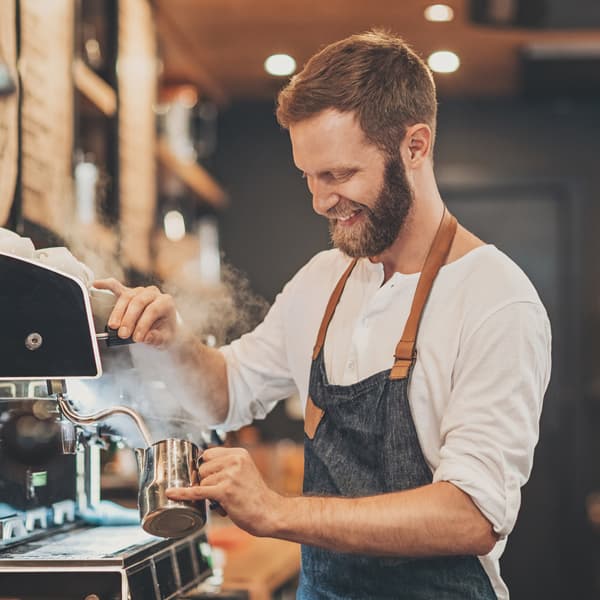 A barista smiling while making a cappuccino in their café.