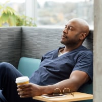 Male nurse with disposable cup resting on sofa in hospital.