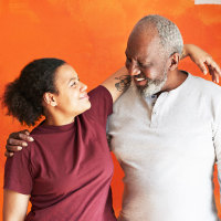 Smiling father and daughter standing with arms around against painted wall at home