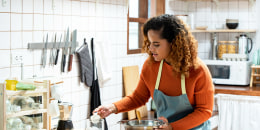 Woman in kitchen learning online virtual cooking class from tablet computer at home.