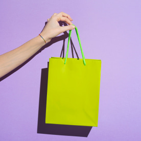 Woman's hand carrying colorful goody bag on lilac background