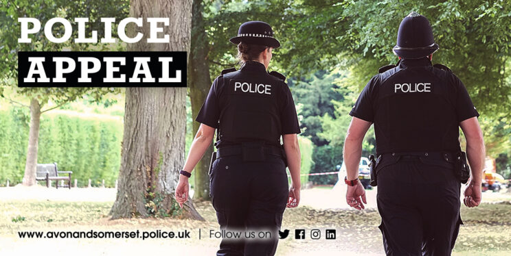 Stock image of a male and female police officer on patrol in a park area with trees.