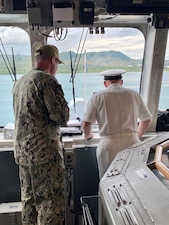 CNO Gilday and the Commanding Officer of USS Charleston look out the windows of the bridge of the ship.