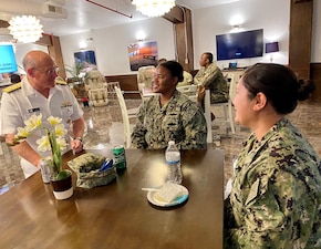 CNO Gilday speaks with two Sailors at a table.