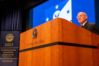 A man in a uniform speaks while he stands behind a podium that reads "U.S. Naval War College" with a banner that reads 2021 International Seapower Symposium.